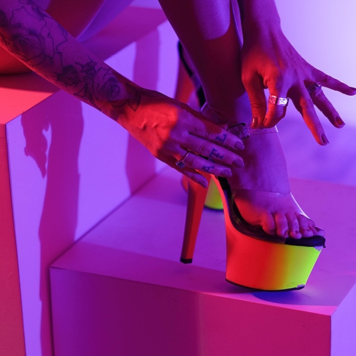 Close up of a tattooed hand strapping on a pair of platform stilettos.